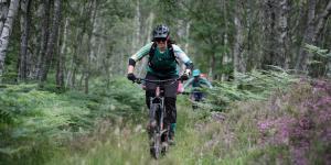 female mountain biker riding through lush green forest in Scotland