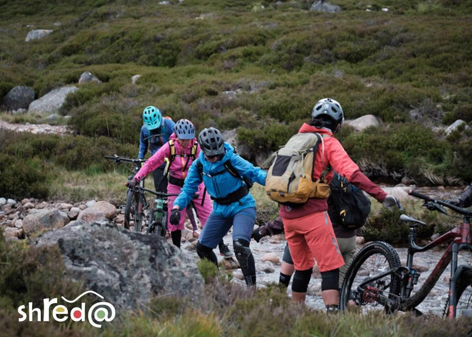 group of female mountain biker crossing a river with their bikes