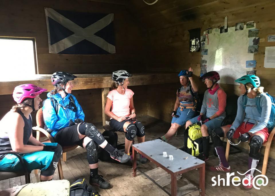 group of female mountain bikers sitting in a bothy and laughing